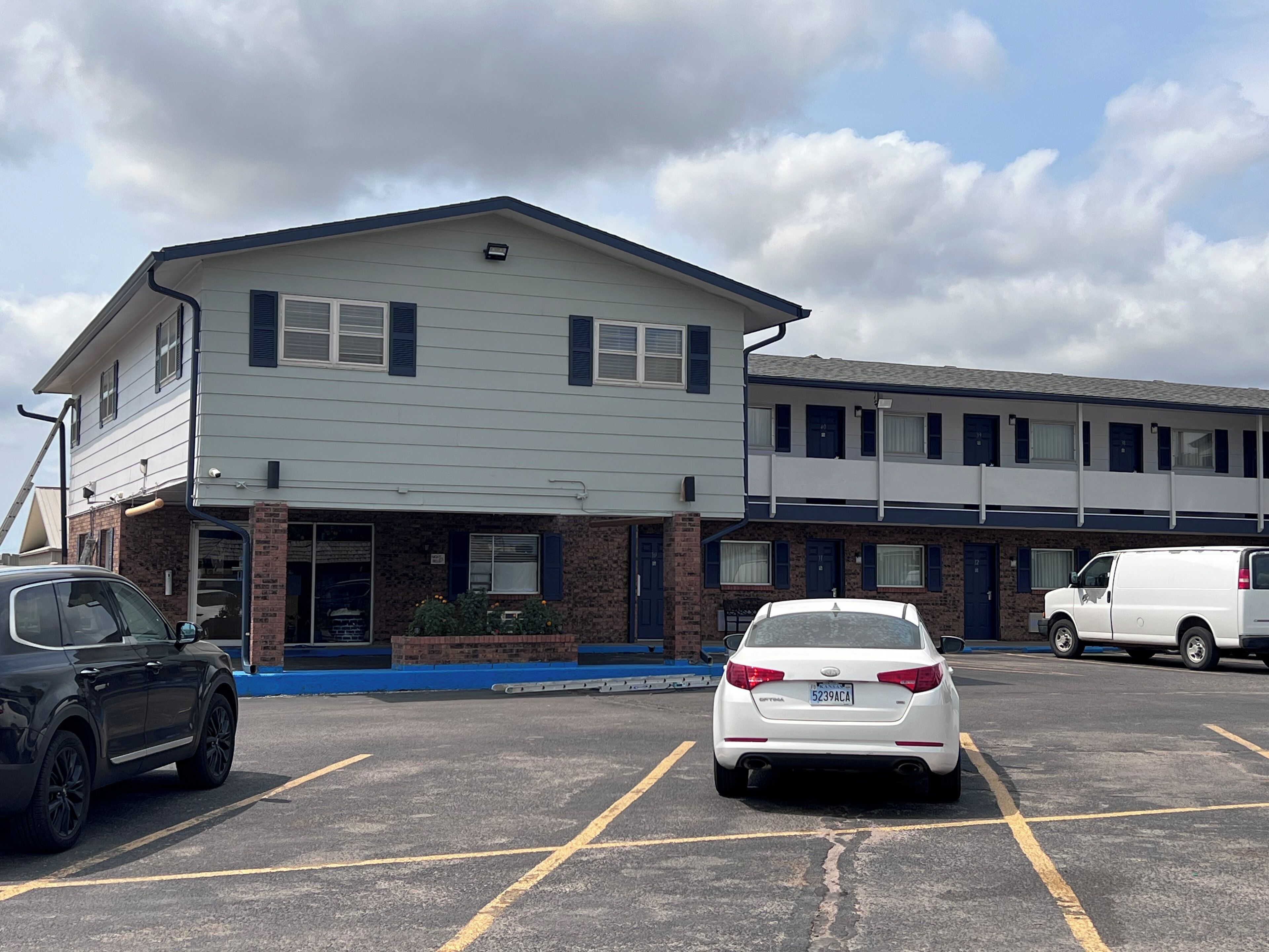 A parking lot with a building that has a flat roof and a brick facade. There are two cars parked in the lot.