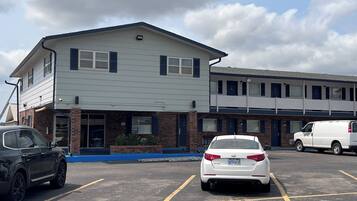A parking lot with a building that has a flat roof and a brick facade. There are two cars parked in the lot.