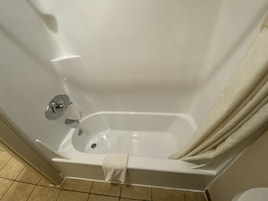 Una bañera blanca con cortina de ducha, una toalla y un grifo cromado.