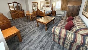 A room with a bed, wooden furniture, a sofa, a table, and a dresser. - Regency Inn and Suites (Dodge City)