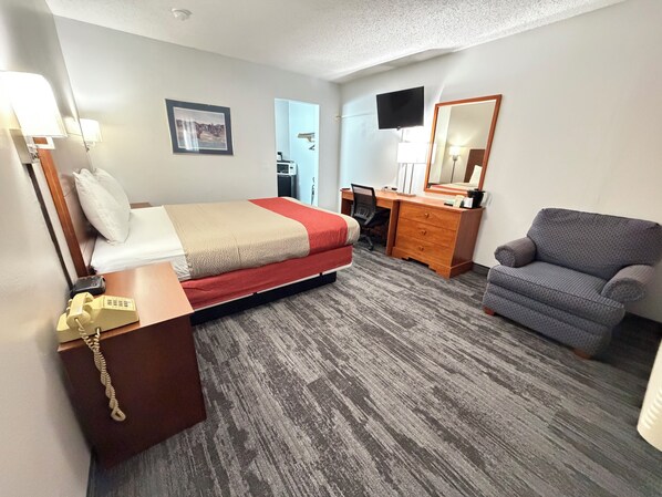 A hotel room with a bed, a desk, a chair, a dresser, a mirror, and a television.