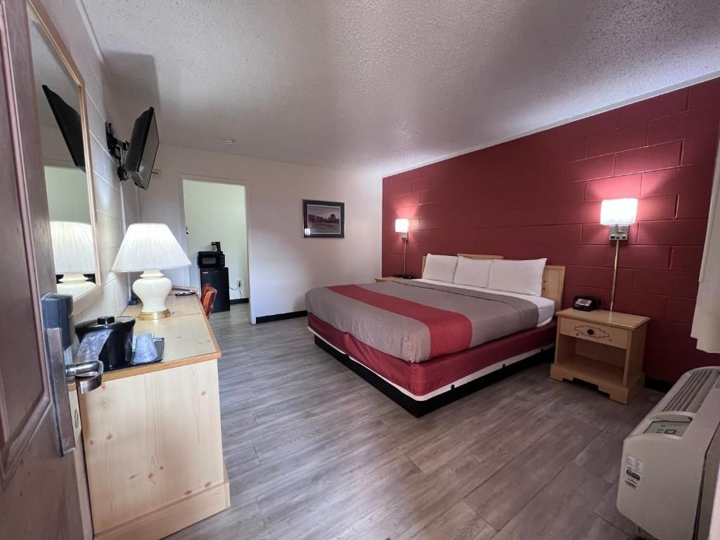 A hotel room with a bed, bedside table, lamp, and a wall-mounted heater.