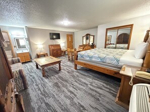 A bedroom with a wooden bed, a desk, a chair, a dresser, a mirror, and a television.