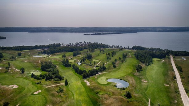 An aerial view of a golf course with multiple holes, water bodies, and a distant shoreline. - Bellmere Winds Resort (Otonabee-South Monaghan)
