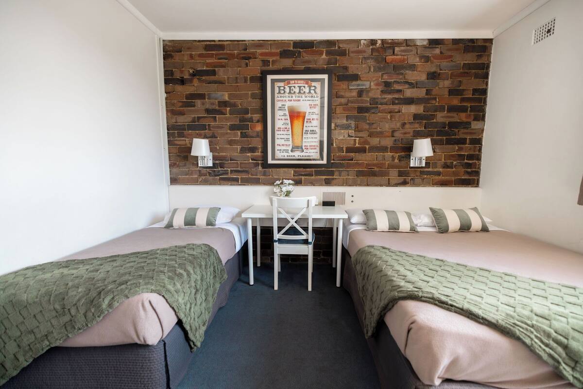 A small room with two beds, a table, and a brick wall.