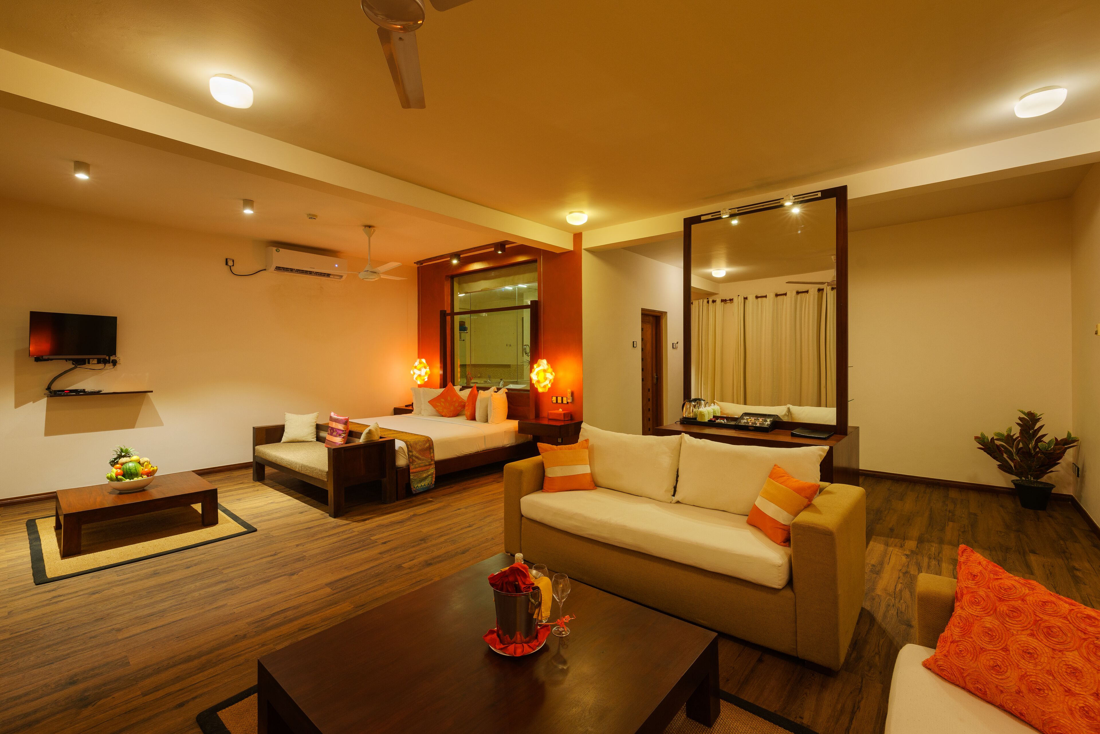 Habitación de hotel con sofá, cama, mesa de centro, televisor y espejo grande.
