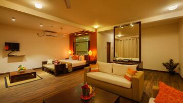 Habitación de hotel con sofá, cama, mesa de centro, televisor y espejo grande.