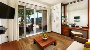 A modern hotel room with a wooden floor, a dining area with a table and chairs, a kitchen area with a counter and appliances, and a large sliding glass door leading to an outdoor area with a view of the sea. - Cocobay Unawatuna (Unawatuna)
