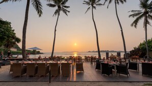 A beachside restaurant with outdoor seating, palm trees, and a view of the sunset over the ocean. - Cocobay Unawatuna (Unawatuna)