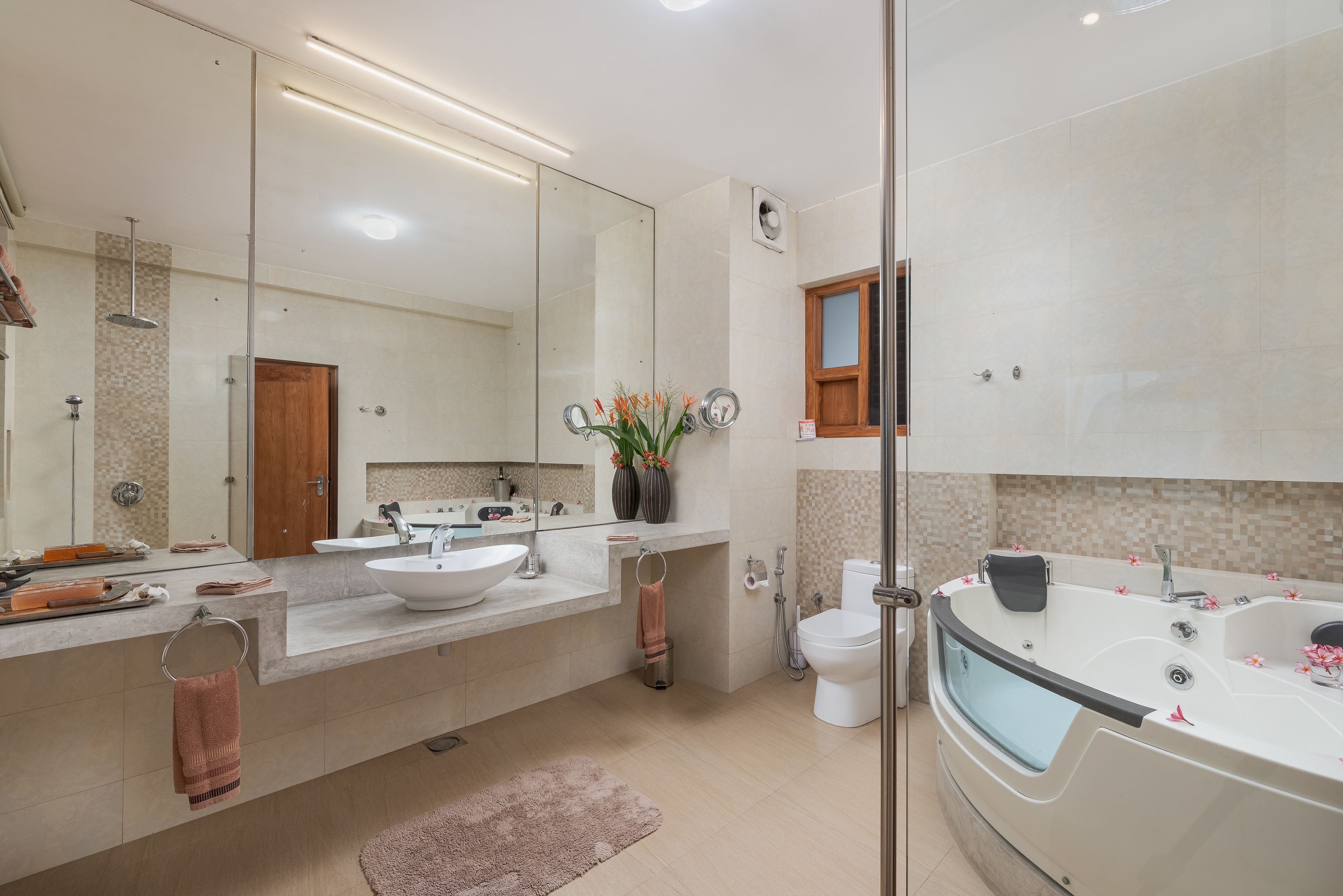 A modern bathroom with a large mirror, a bathtub, a sink, and a toilet.