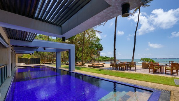 An infinity pool with a clear view of the ocean, outdoor seating, and palm trees. - Cocobay Unawatuna (Unawatuna)