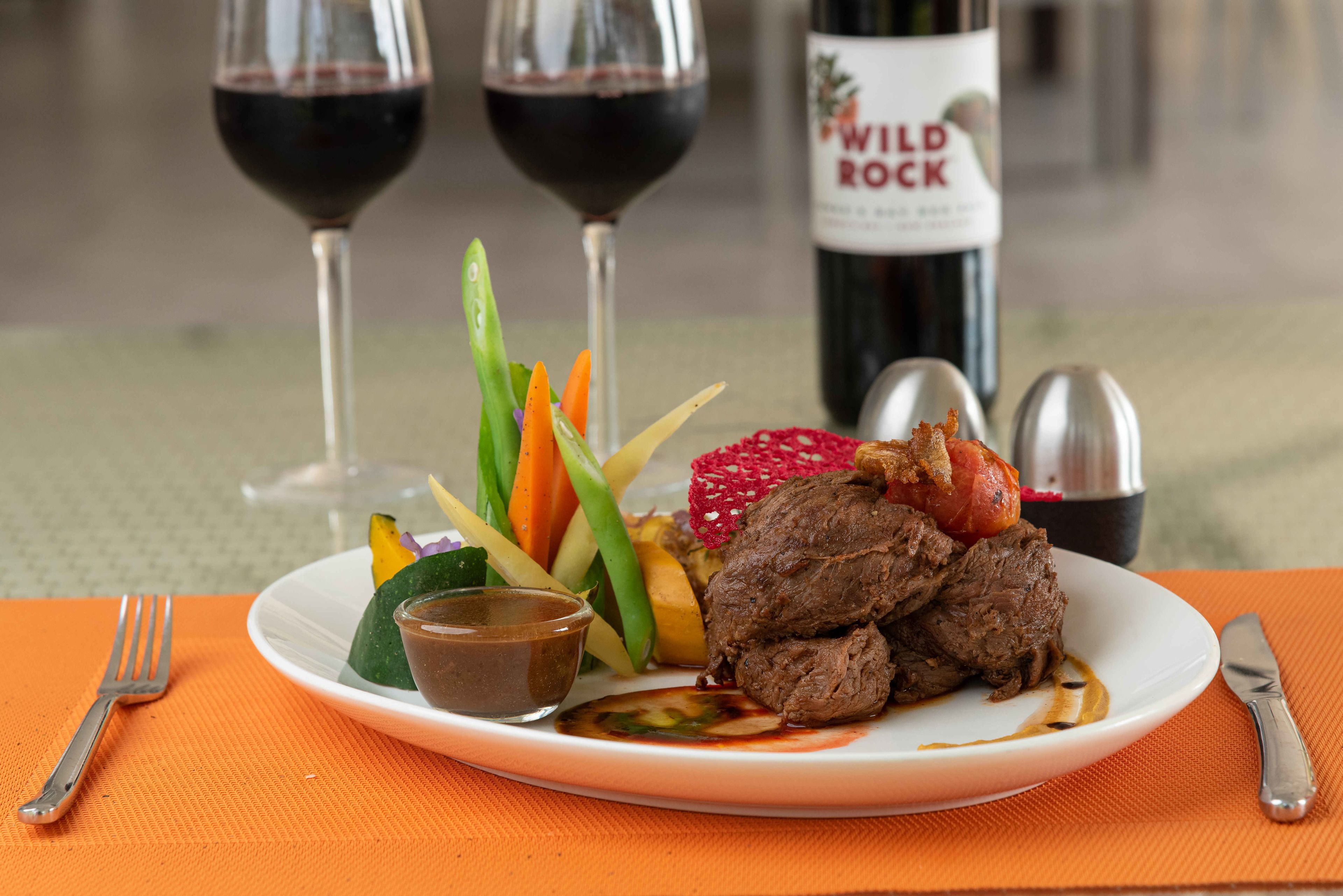 A plate of food with a bottle of wine and glasses in the background.