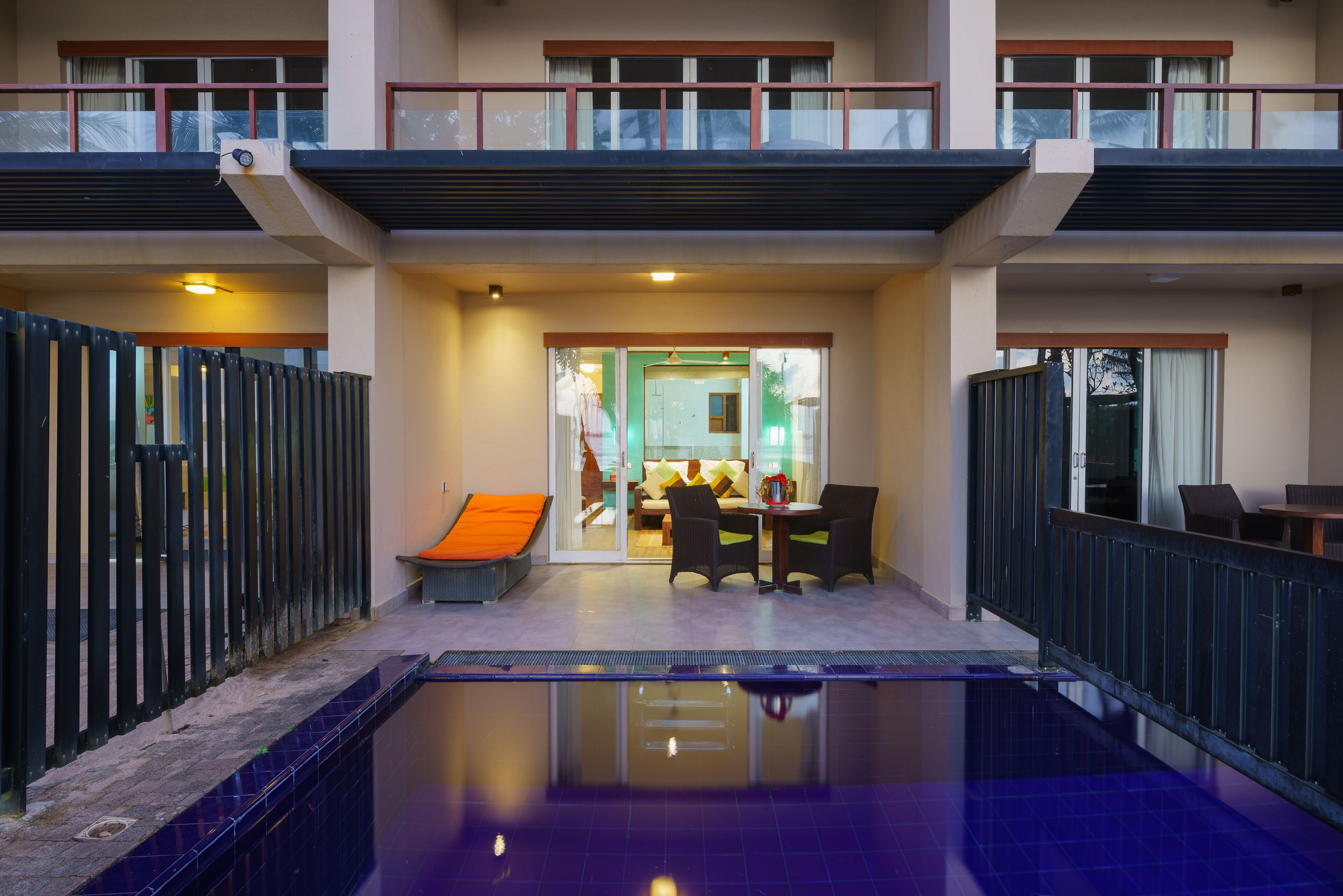 A hotel with a pool area, a dining area with chairs and a table, and a balcony with railings.