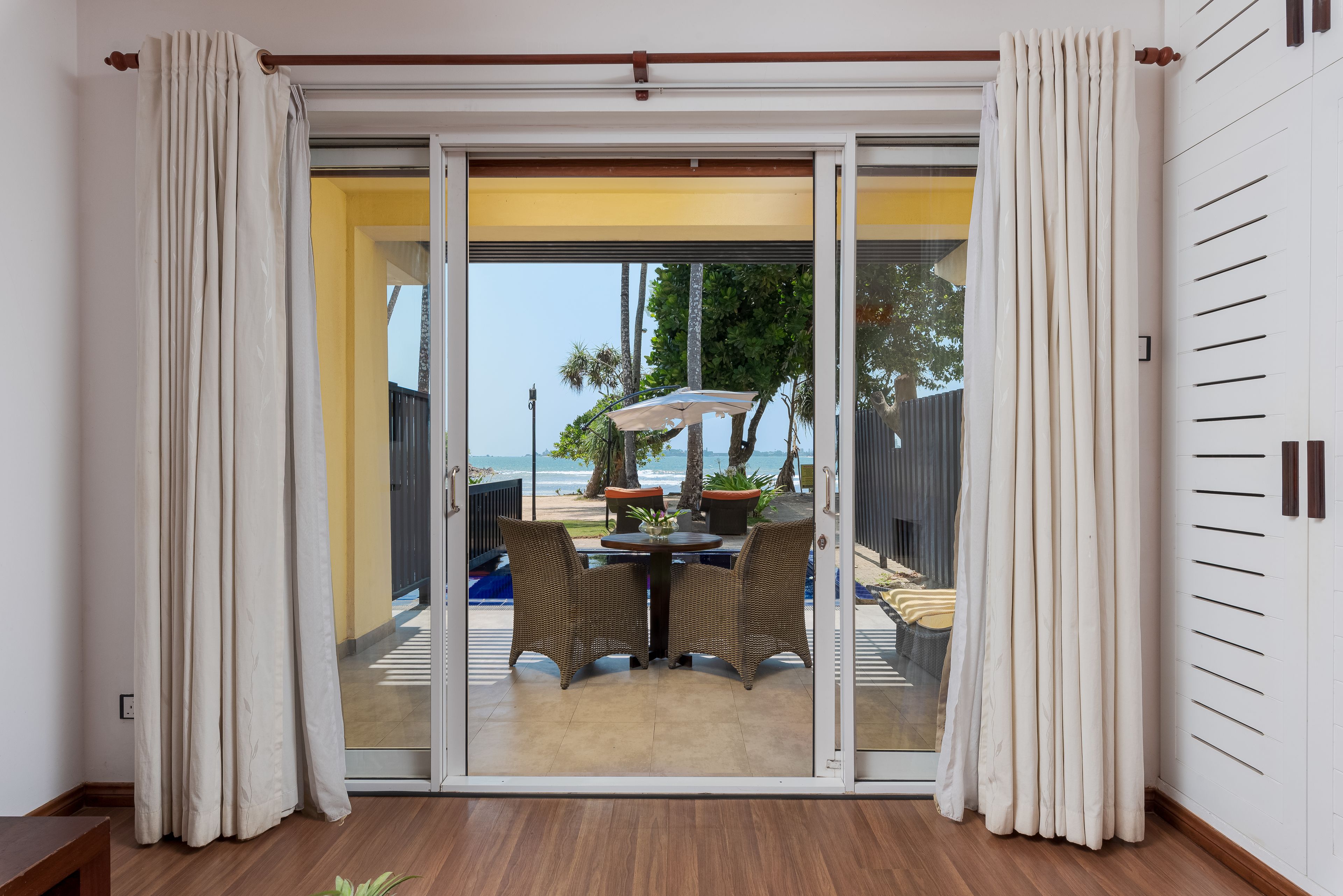A room with a sliding glass door leading to a balcony with outdoor furniture and a view of the ocean.