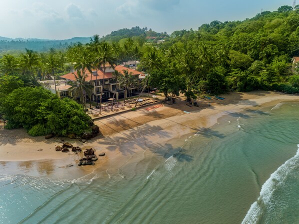A beachfront property with a pool area, palm trees, and a view of the ocean.
