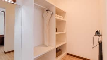 A walk-in closet with white shelving, a hanging robe, and a pair of slippers.