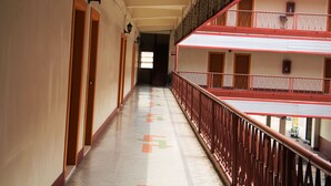 A corridor with a red railing, doors on the left, and a multi-story building on the right. - Phu Inn Hotel (Khon Kaen)