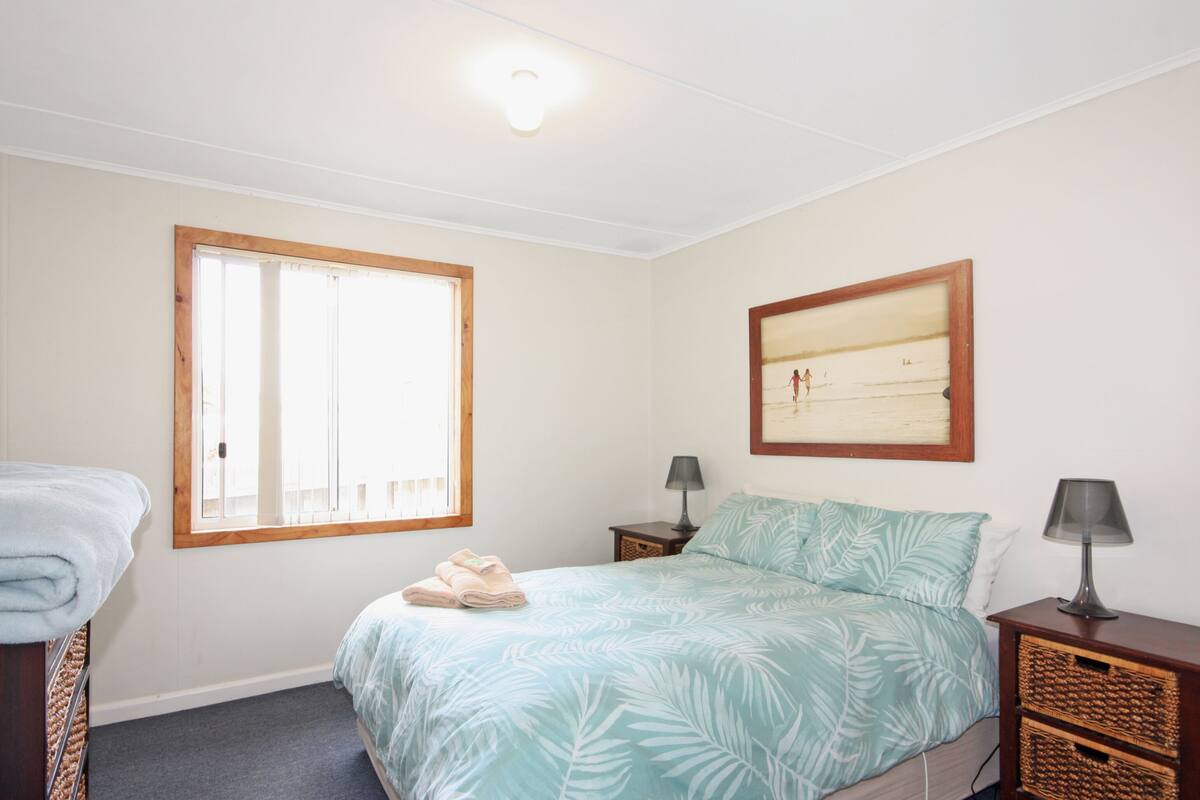 A bedroom with a bed, two bedside tables, a window, and a framed picture on the wall.