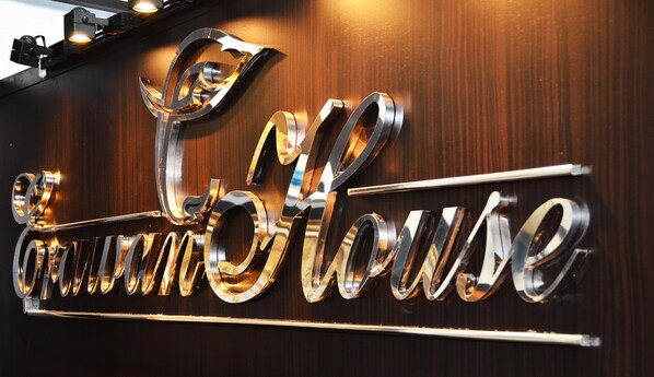 A metallic sign with the words "CrownHouse" in a stylized font, mounted on a wooden wall. - Erawan House (Bangkok)