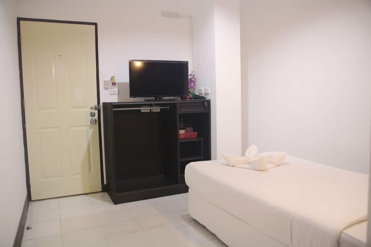 Een hotelkamer met een bed, een televisie op een standaard, een kledingkast en een deur.
