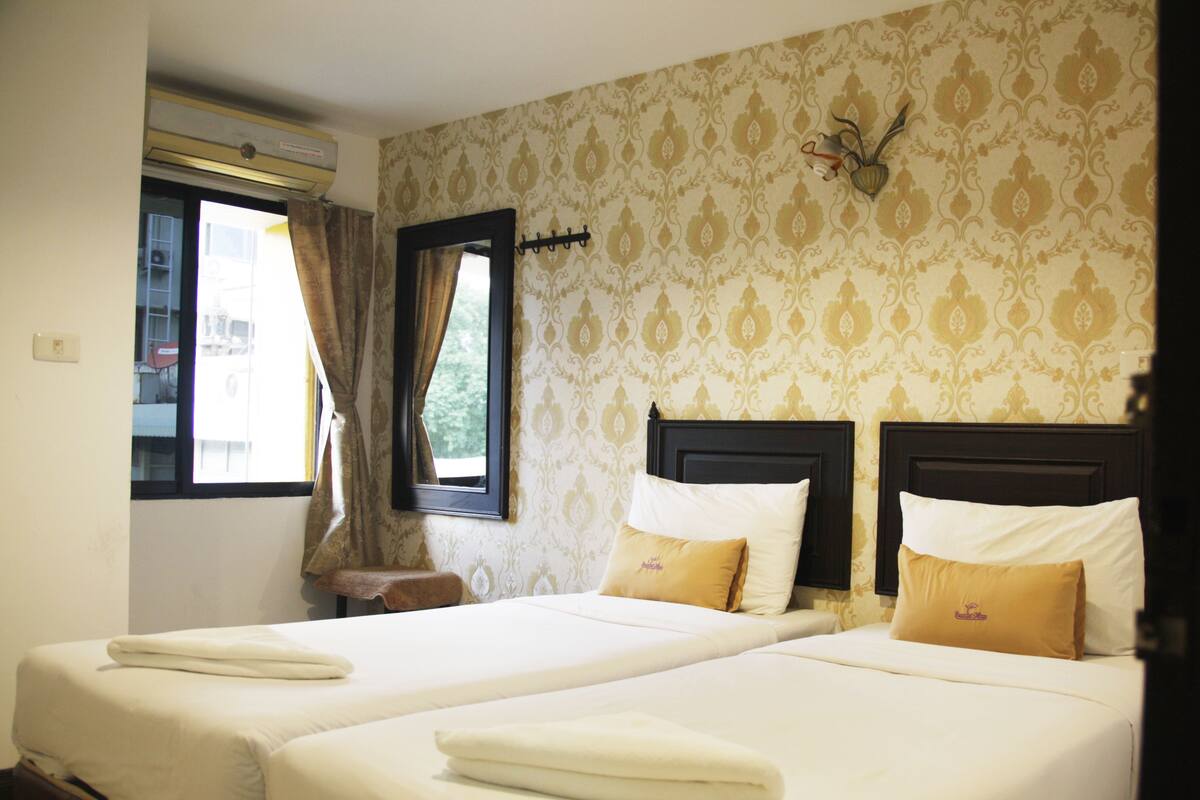 Een hotelkamer met twee bedden, een raam met gordijnen, een hangplant en een kleine tafel.