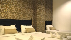 Quarto de hotel com duas camas, cada uma com roupa de cama e almofadas brancas. O quarto possui papel de parede estampado e uma cabeceira escura.
