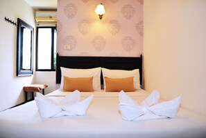 A hotel room with a neatly made bed, a wall-mounted light fixture, and a window with a view. - Erawan House (Bangkok)