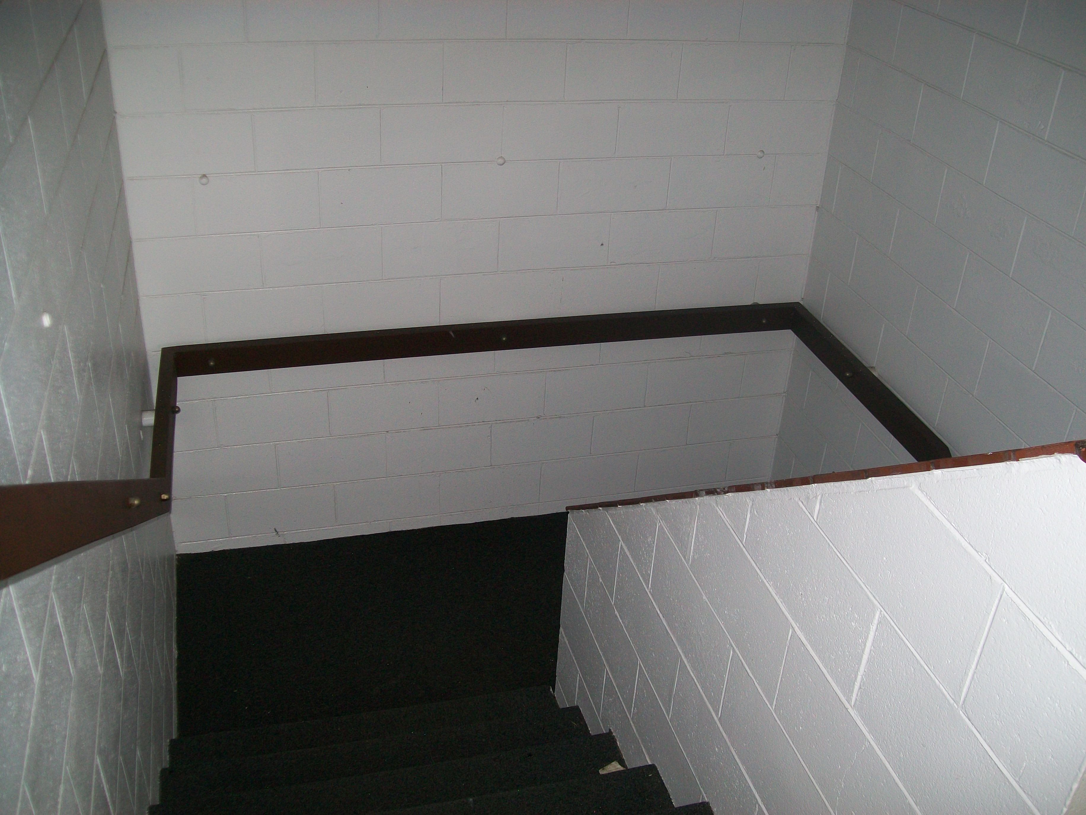 A narrow stairway with white tiled walls and a dark carpeted floor.