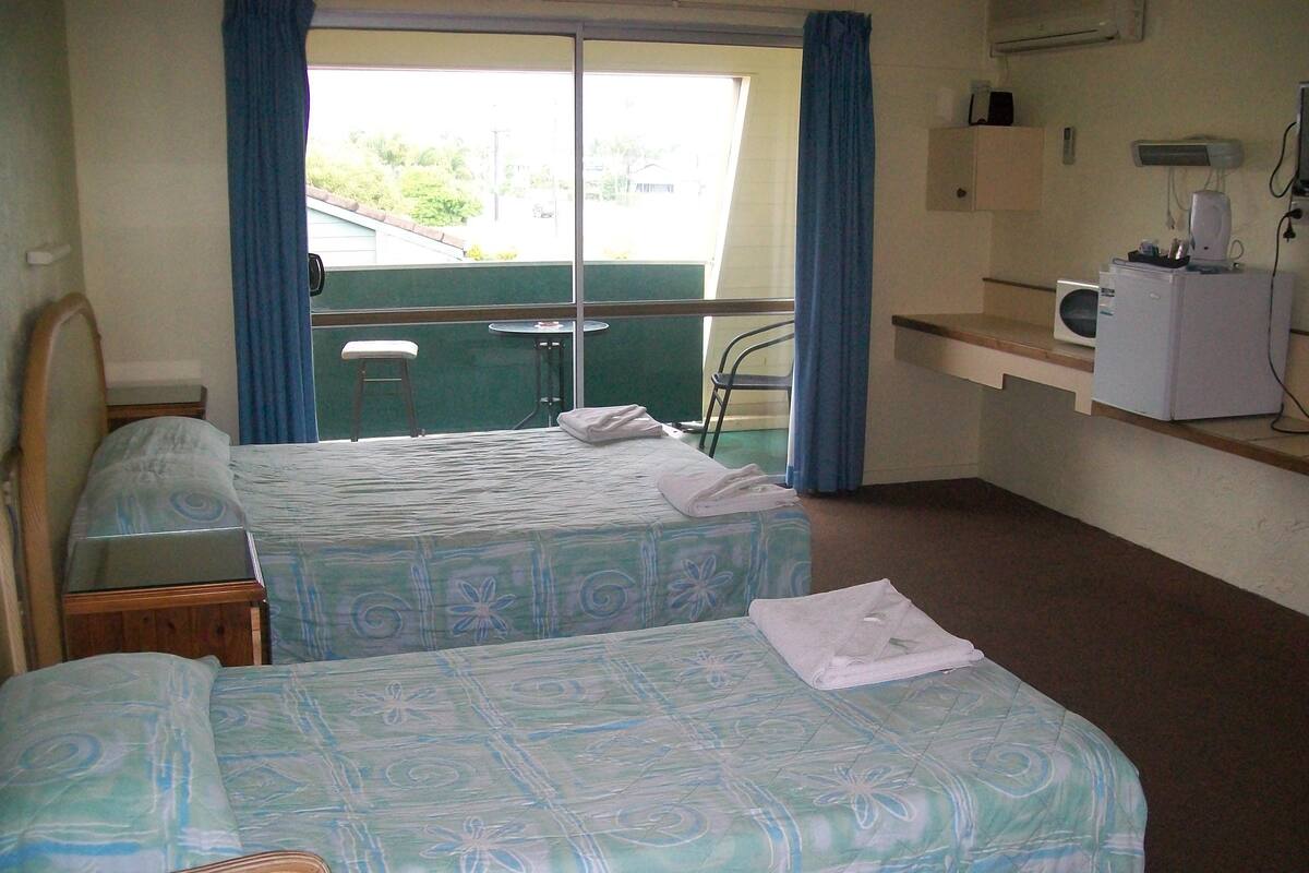 A hotel room with two beds, a small desk, a chair, a microwave, and a window with curtains.