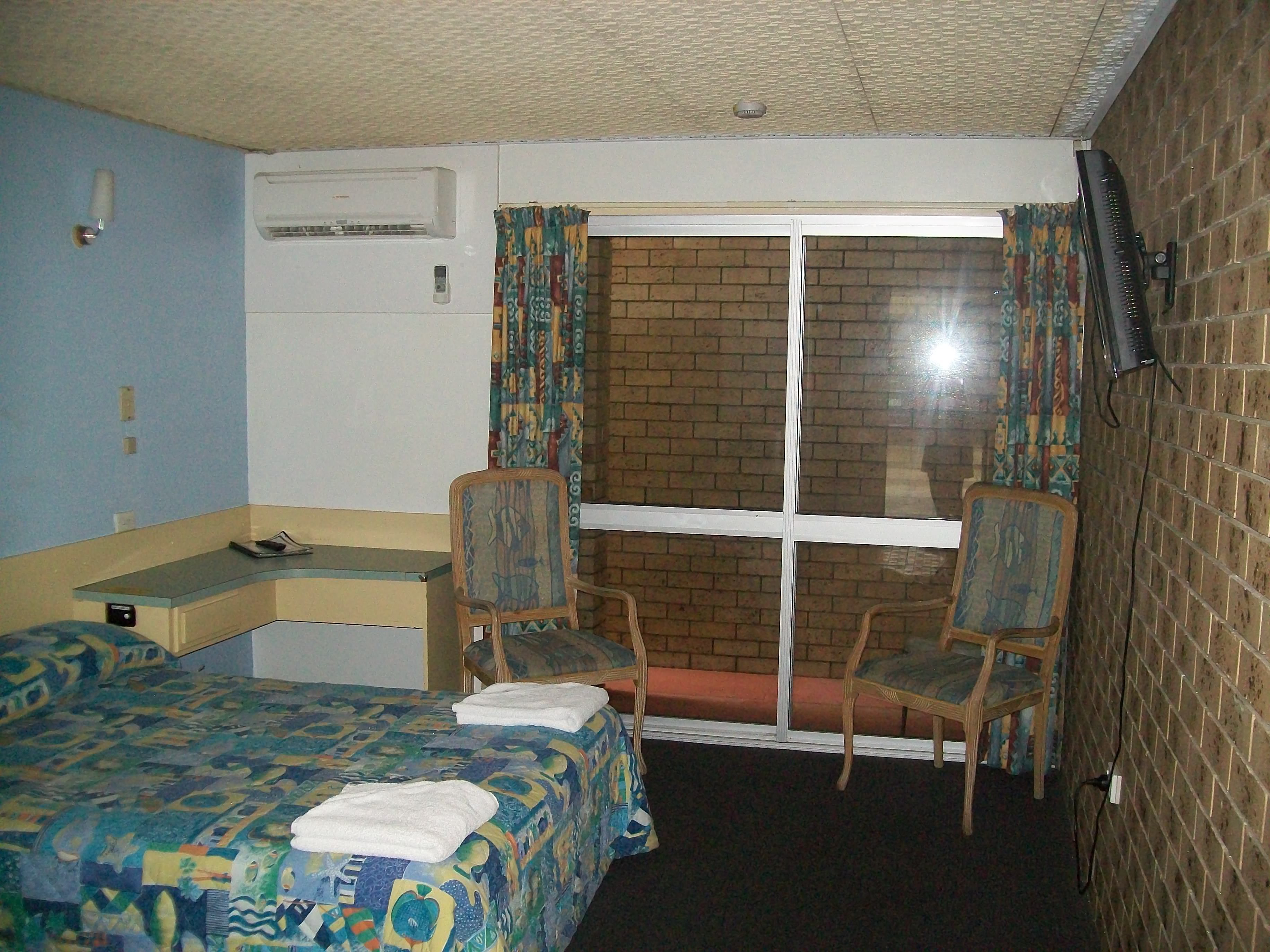 Une chambre d’hôtel avec un lit, deux chaises, un bureau, un climatiseur et une fenêtre avec des rideaux.