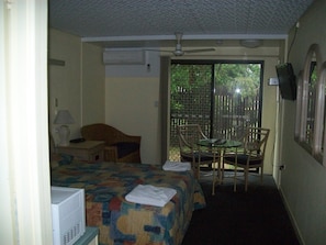 Ein Hotelzimmer mit einem Bett, einem Schreibtisch mit Lampe, einem Fernseher, einem Sessel und Blick ins Freie.