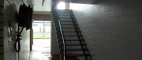 A stairwell with a metal handrail, a wall-mounted telephone, and a visible exit door leading outside.
