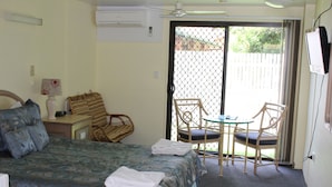 A hotel room with a bed, a desk with a lamp, a chair, a table, and a sliding glass door leading to an outdoor area. - Sun Plaza Motel Mackay (West Mackay)