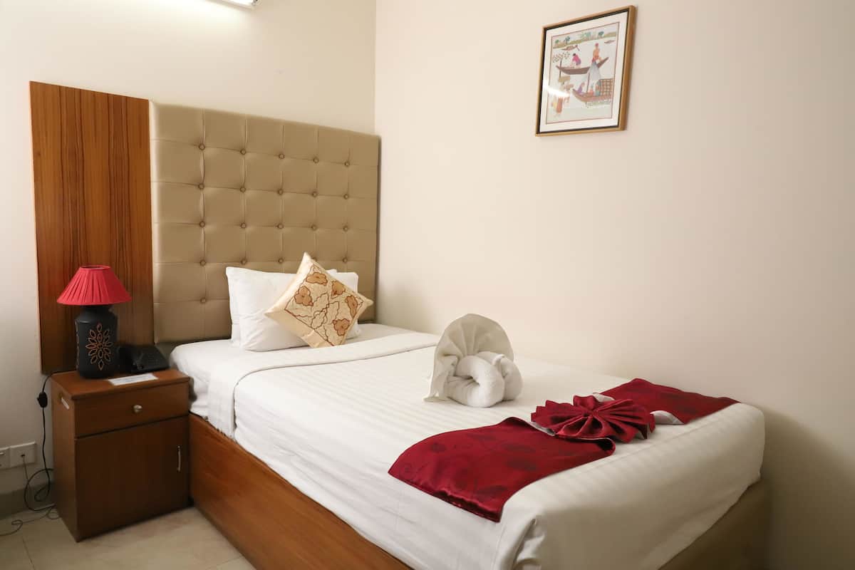 A neatly made bed with white and red linens, a wooden nightstand with a lamp, and a framed picture on the wall.