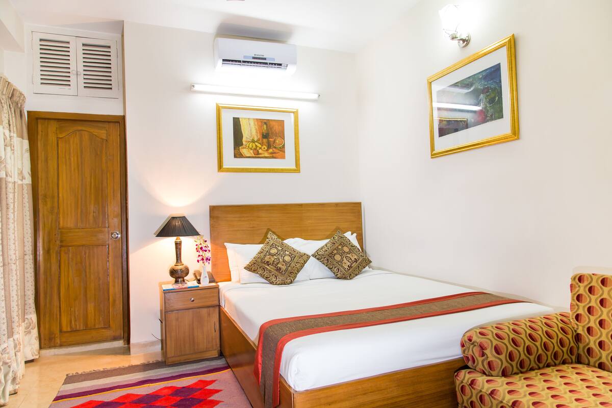 A neatly arranged bedroom with a wooden bed, a nightstand, a lamp, and a patterned chair.