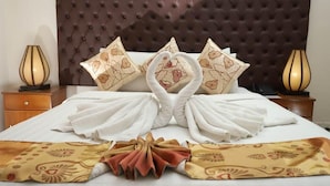 Una habitación de hotel con un cabecero capitonado, una cama con toallas dispuestas en forma de cisne y dos lámparas de noche.