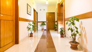 Un pasillo de hotel con puertas de madera, plantas en macetas y un suelo de mármol.