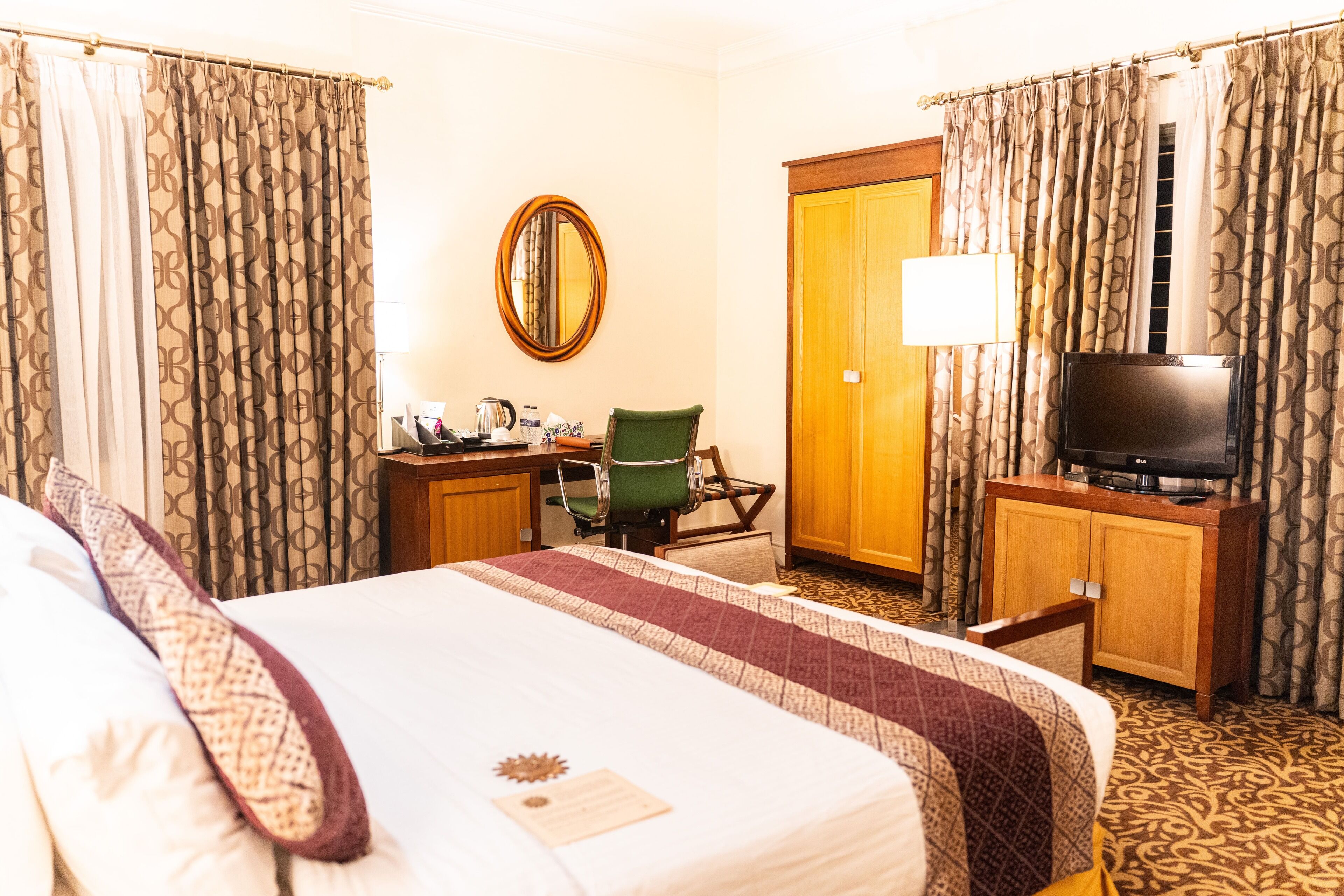 A hotel room with a large bed, a desk with a chair, a television, and a wardrobe.