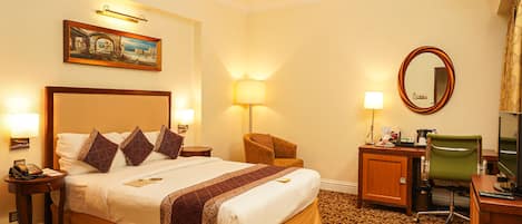 A hotel room with a large bed, a desk, a chair, a desk lamp, a telephone, and a painting on the wall.