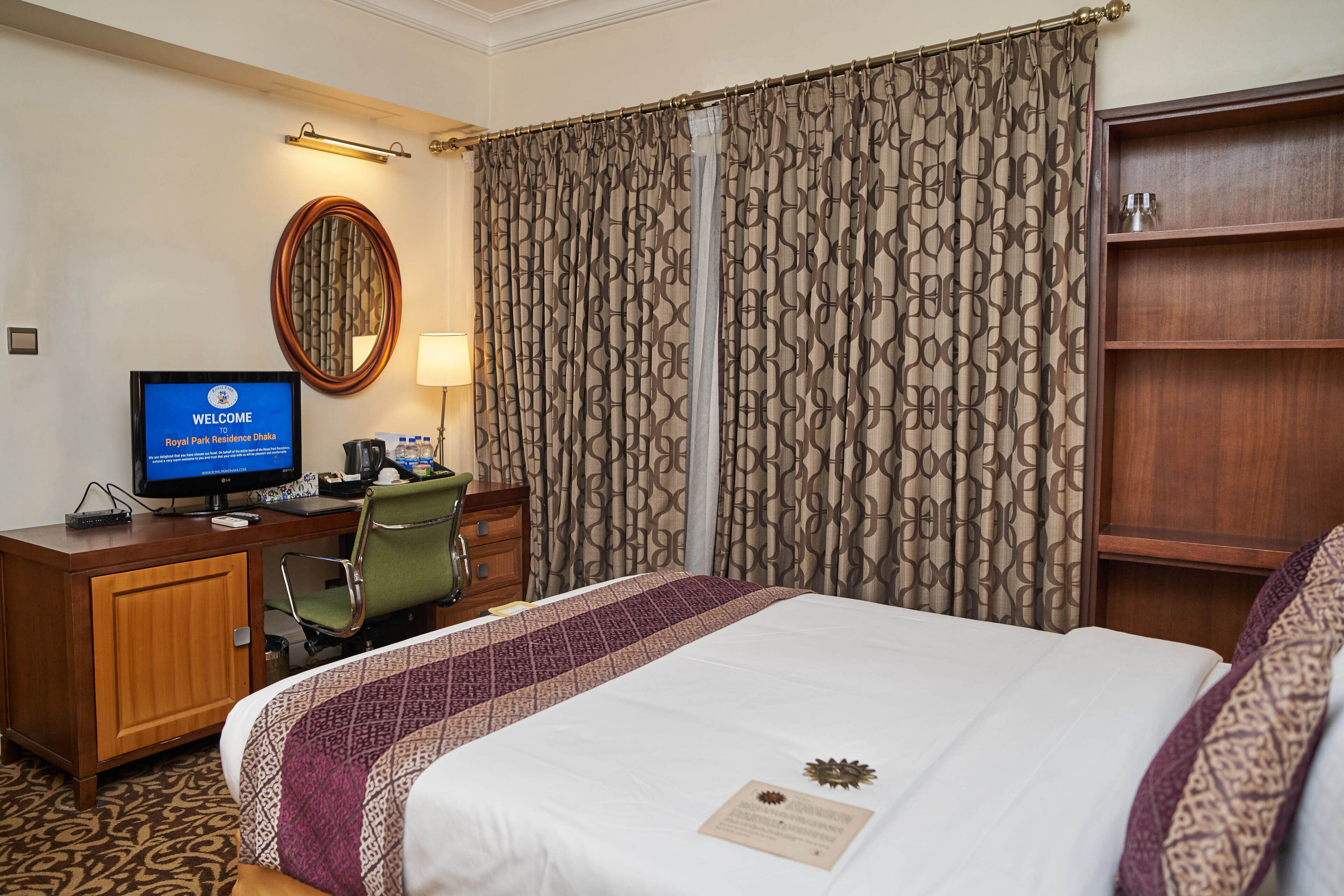 Habitación de hotel con cama, escritorio con computadora, silla, armario y cortina de estampado geométrico.