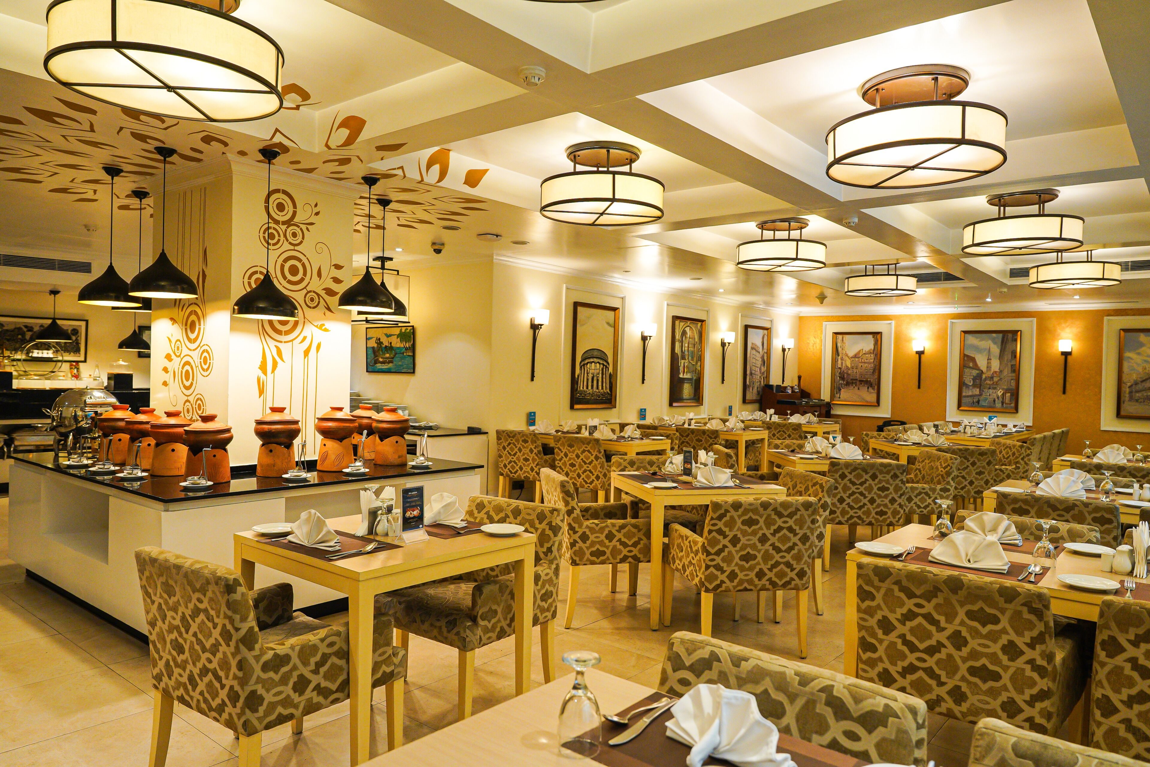 A restaurant with multiple tables and chairs, featuring a central island with a buffet setup.