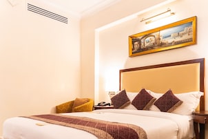 Habitación de hotel con una cama grande, cabecero, un cuadro en la pared, mesita de noche y una silla.