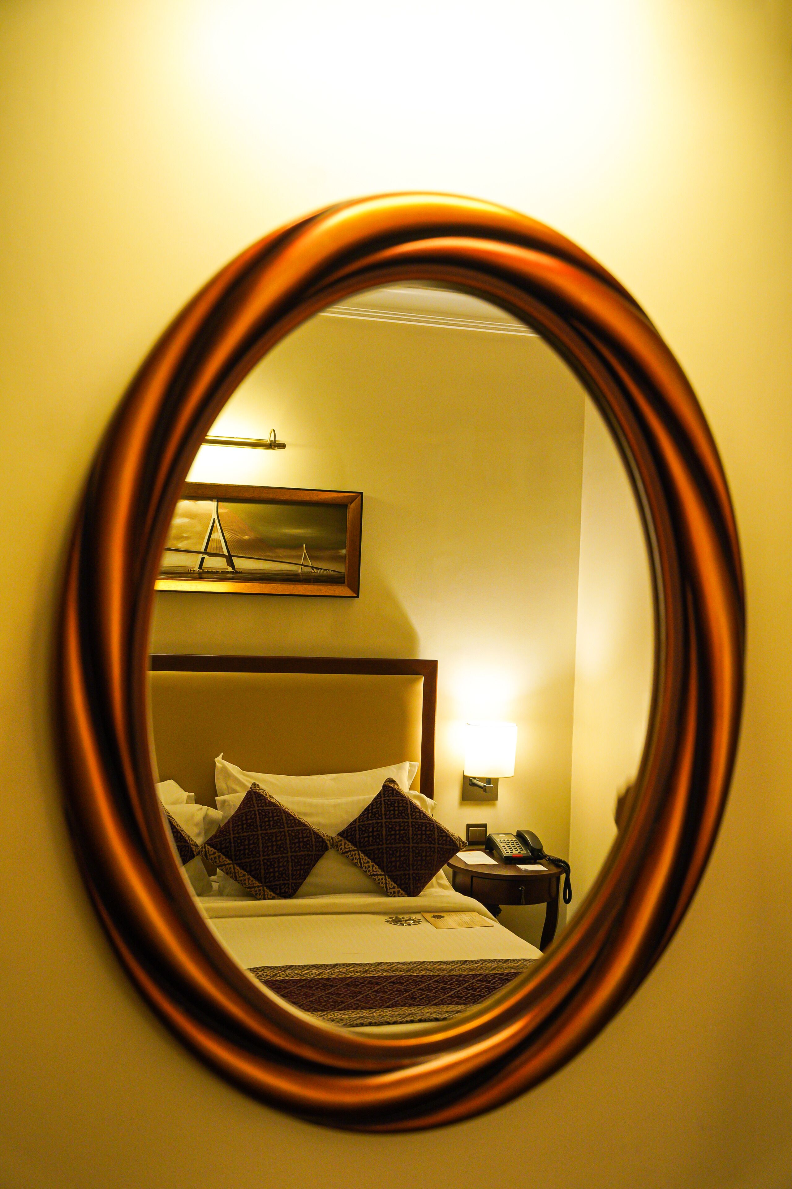 A hotel room with a bed, a nightstand, a lamp, and a painting on the wall.