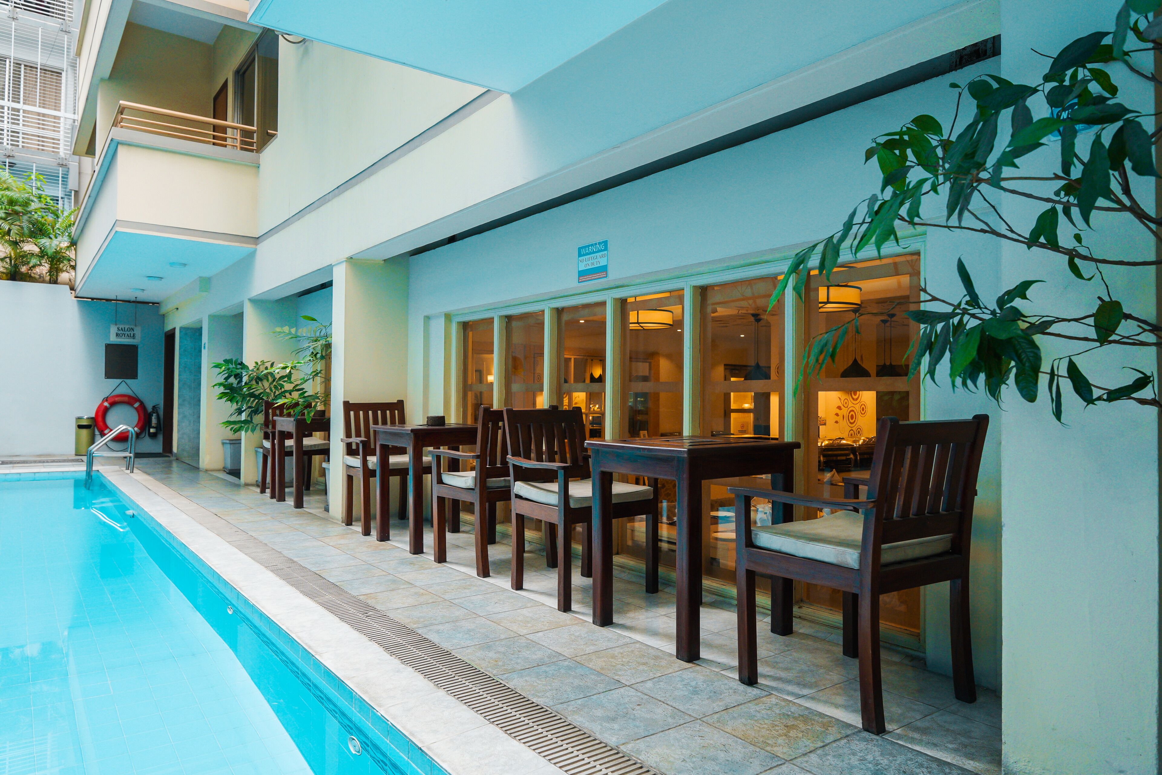 A swimming pool with adjacent outdoor seating and a building with large windows.