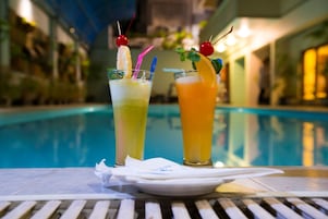 Dos cócteles con guarniciones de frutas y pajitas sobre una mesa junto a una piscina.