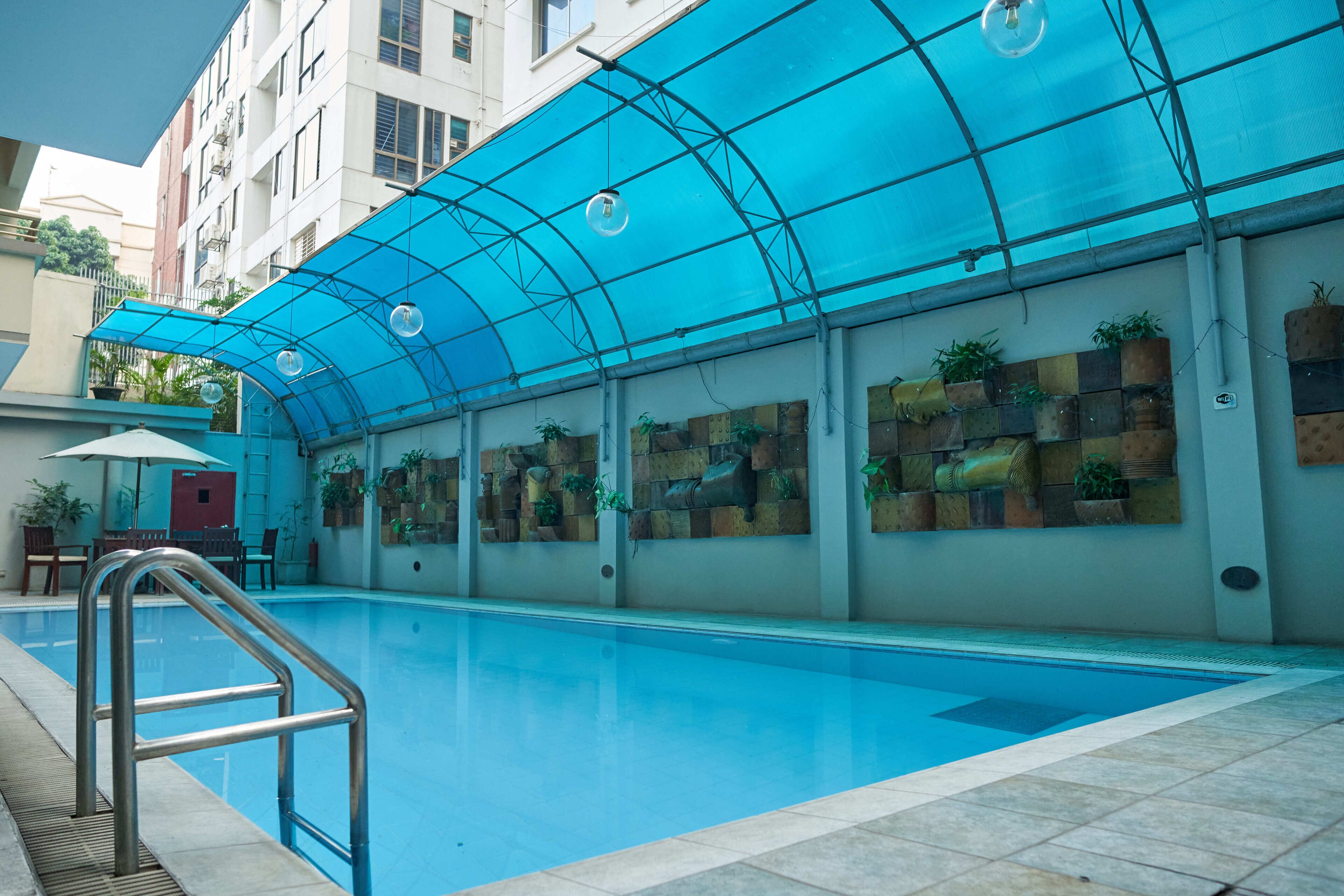 A swimming pool with a blue canopy, surrounded by potted plants and a tiled floor.