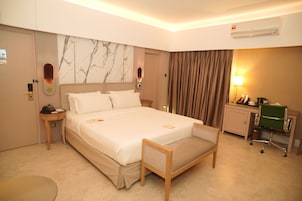 Habitación de hotel con una cama grande, mesitas de noche, un escritorio, una silla y un equipo de aire acondicionado.