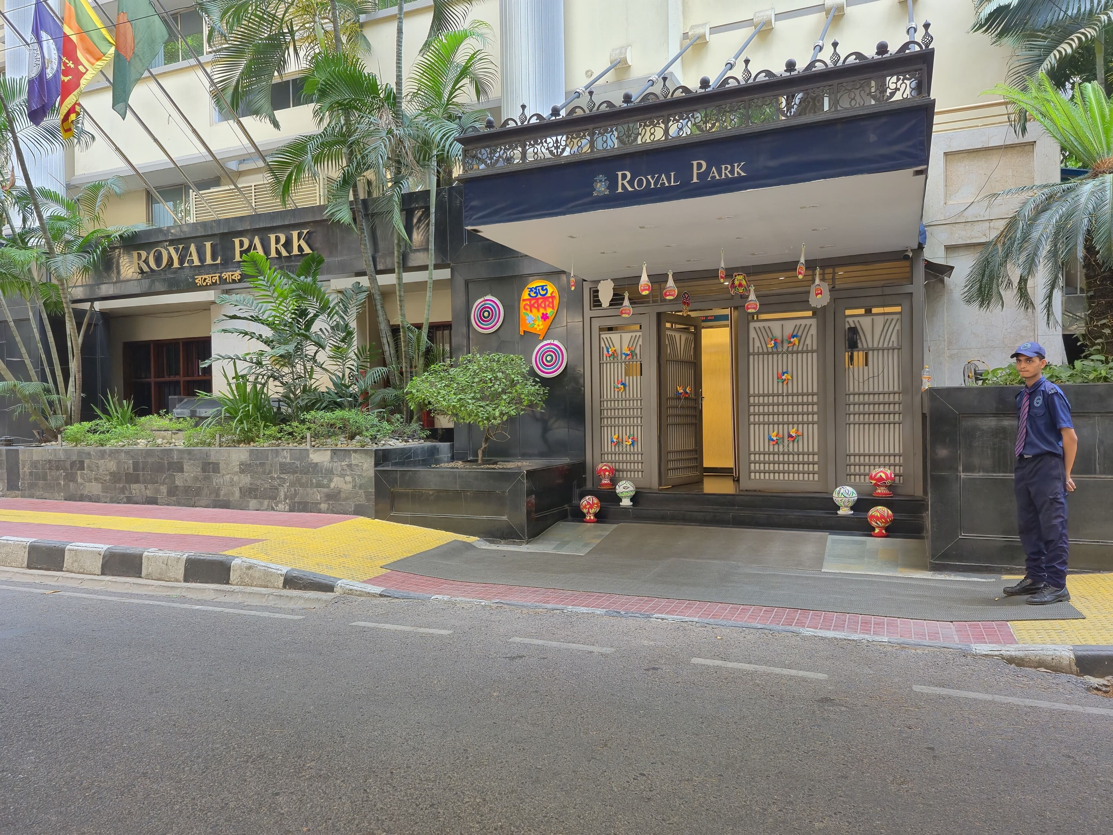 The entrance of a hotel named "Royal Park" with a traditional design, including a signboard, decorative elements, and a security guard standing outside.