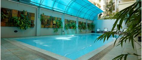 Una piscina interior con techo de vidrio, rodeada de paredes decoradas con plantas y obras de arte.