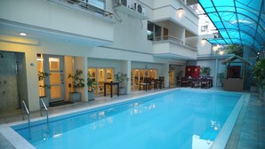 An indoor swimming pool with a glass ceiling, surrounded by seating areas and a reception desk.